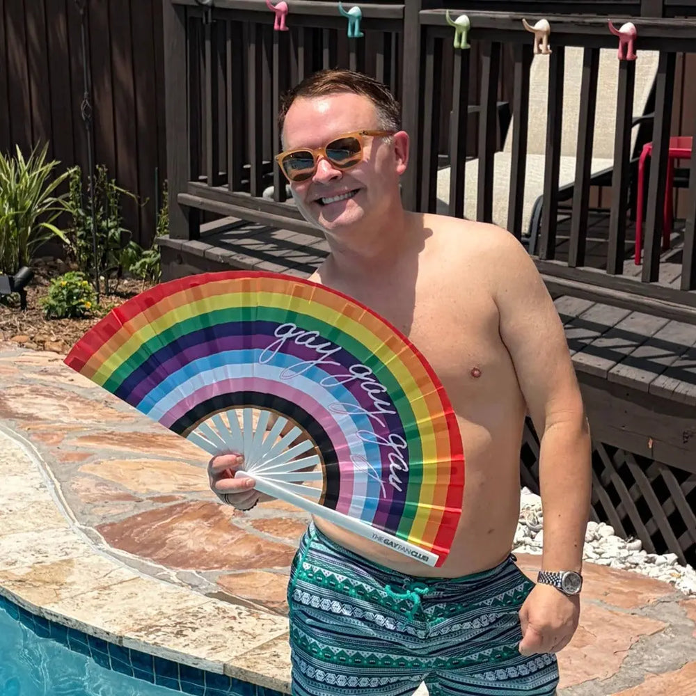 man holding a rainbow clack fan with "gays, gays, gays" written on it in cursive 