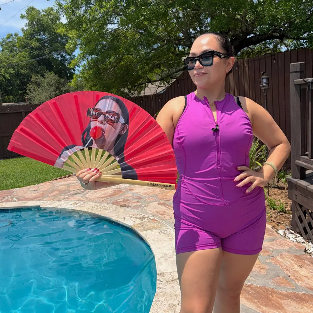 Woman in purple swimsuit holding a red fan by a pool