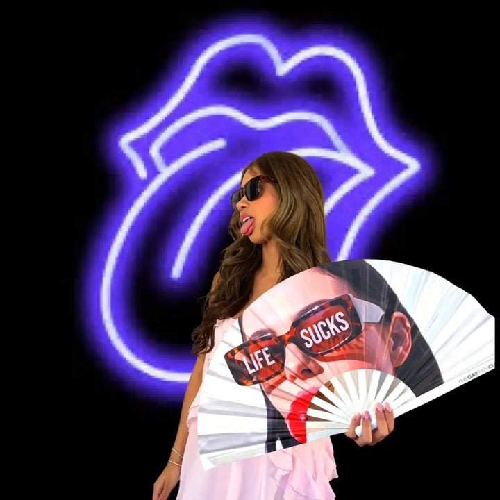 Woman holding a fan with graphic design in front of a neon sign of lips.