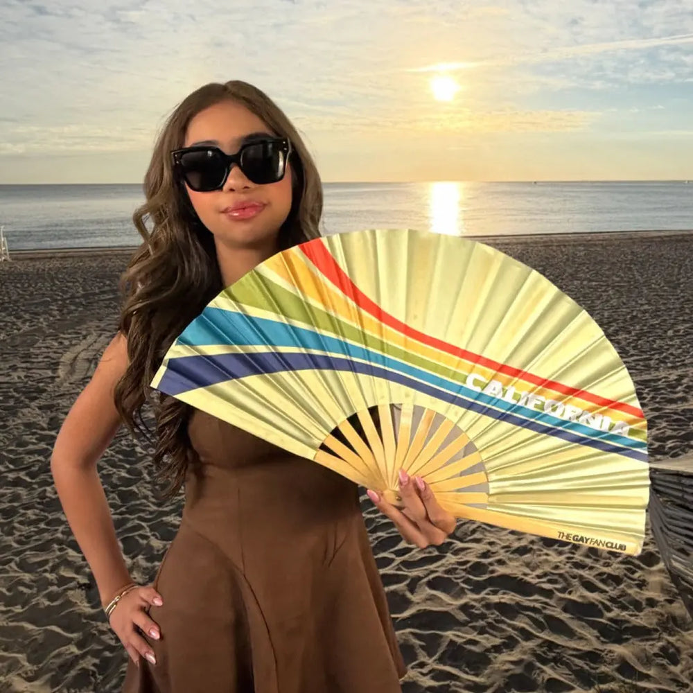 Woman holding a colorful fan on a beach at sunset