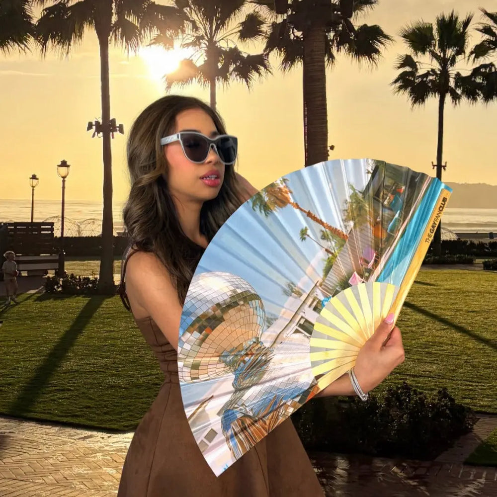 Woman holding a fan with scenic images in a park setting