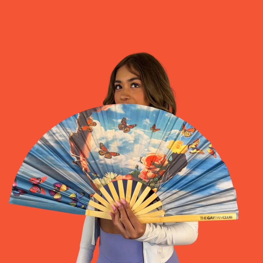 Woman holding a colorful hand fan with butterfly design against an orange background