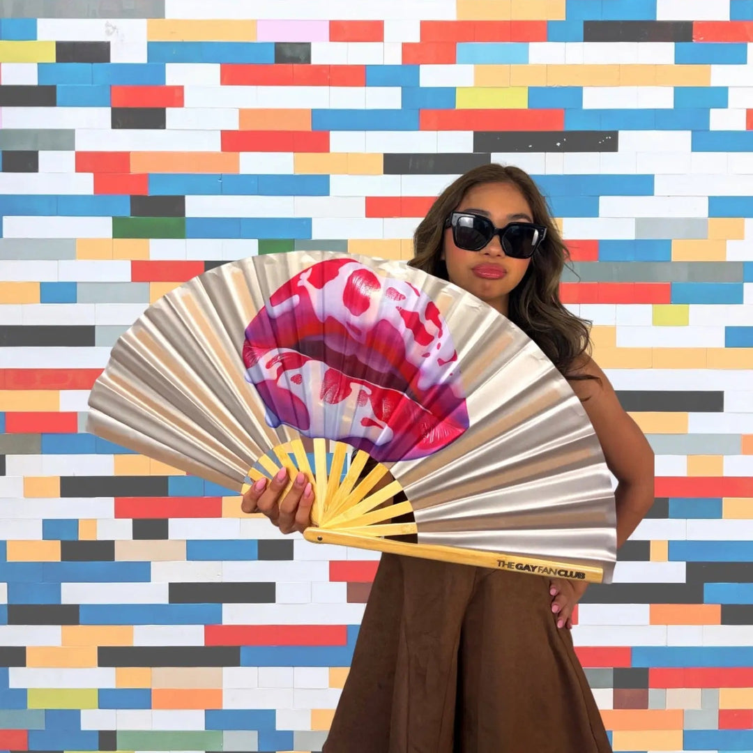 Woman holding a colorful fan in front of a multicolored geometric wall.