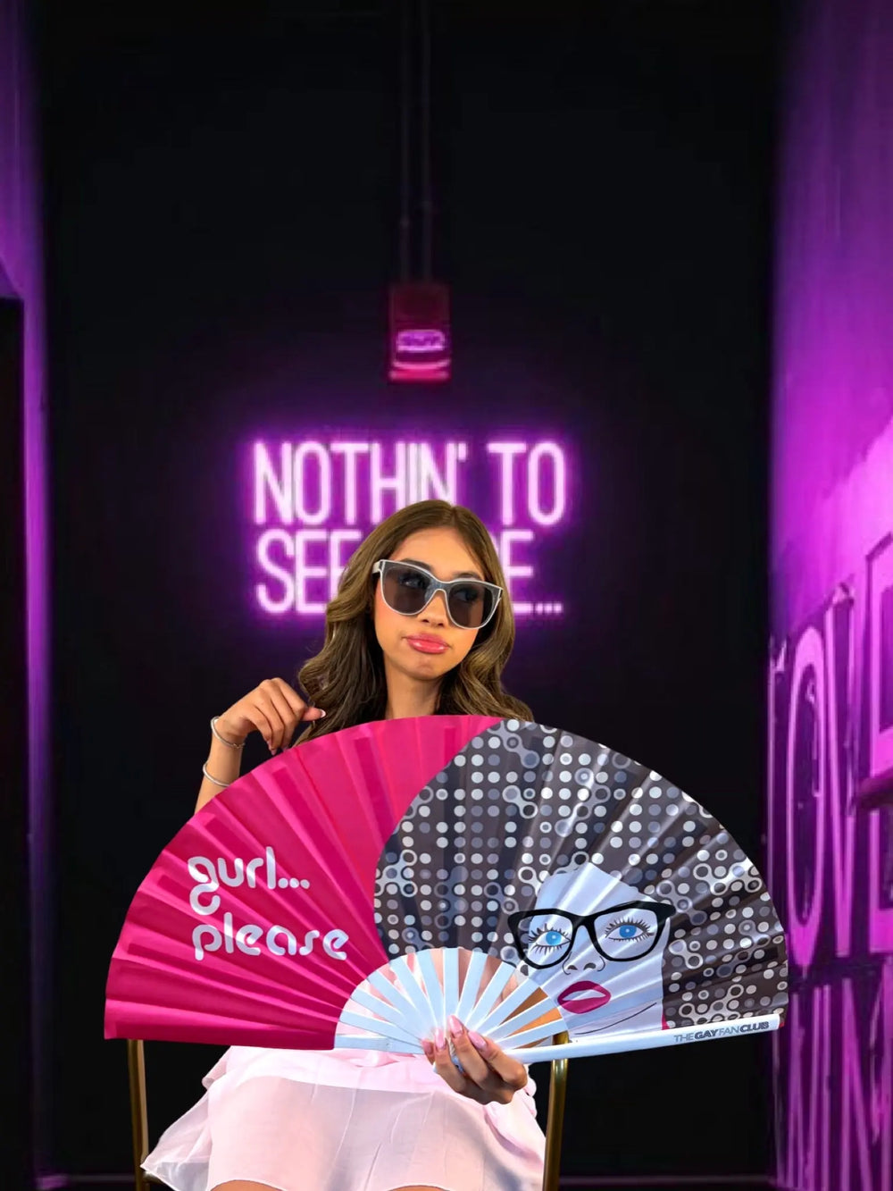 Woman holding a fan with text in front of a dark background with neon signs.