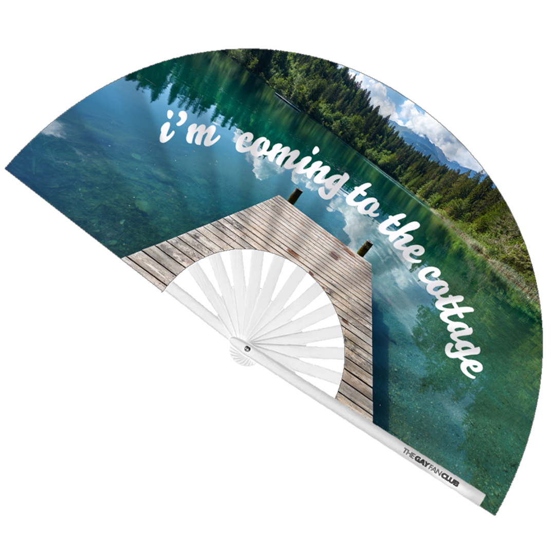 I'm Coming to the Cottage" fan fully open showing a serene lake and dock with white cursive text on a white bamboo frame.Clack Fan