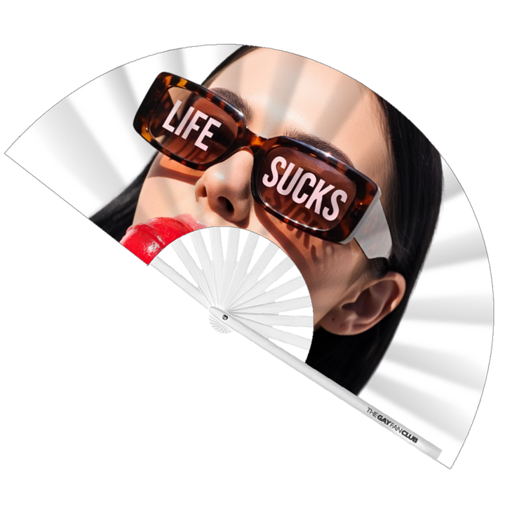 Life Sucks Fan fully open showing a woman in tortoise-shell sunglasses with "LIFE SUCKS" text on the lenses, holding a red lollipop, set against white bamboo ribs.