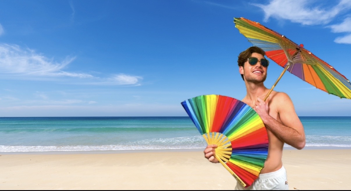 Man on a beach holding a colorful umbrella and rainbow bamboo clack fan from The Gay Fan Club with blue sky and ocean in the background