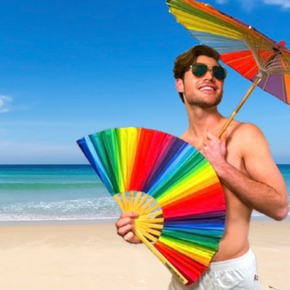 Man holding a colorful umbrella and fan on a beach