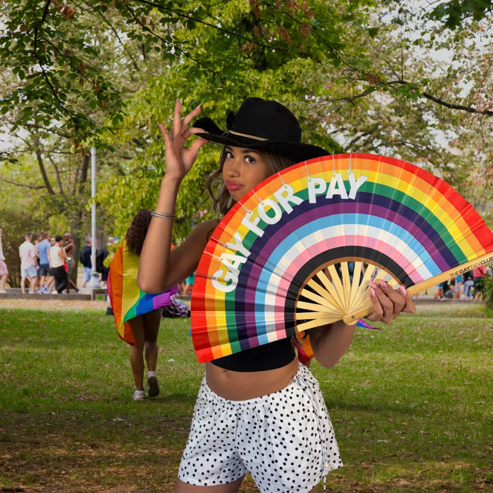 Woman holding a rainbow clack fan with the message "Gay For Pay" 
