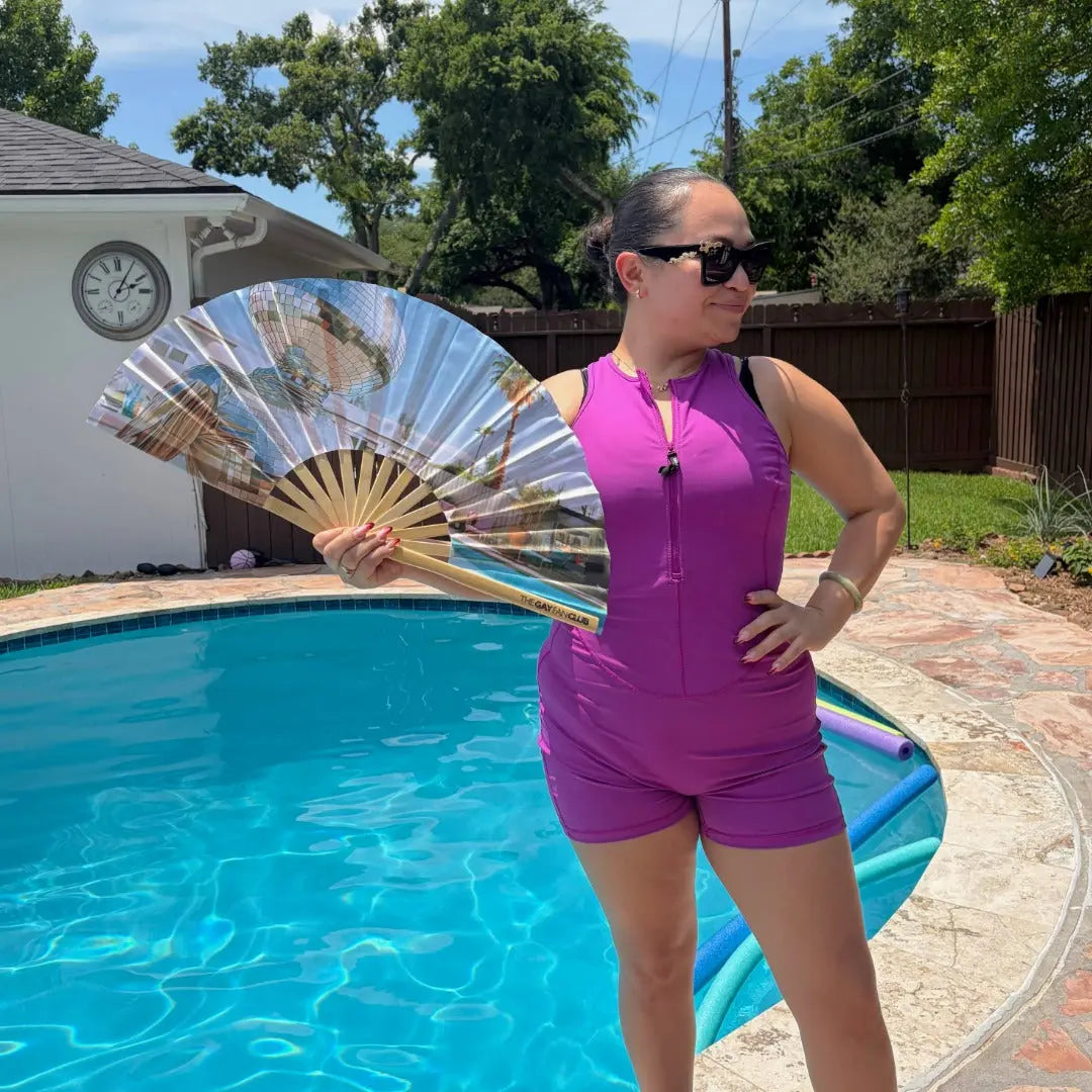 Woman in purple swimsuit holding a decorative fan by a pool